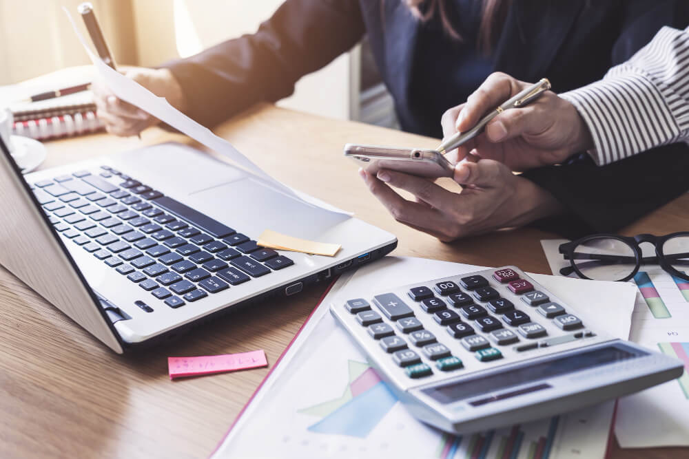 Pessoa calculando o DRE em frente ao computador e com calculadora ao lado.