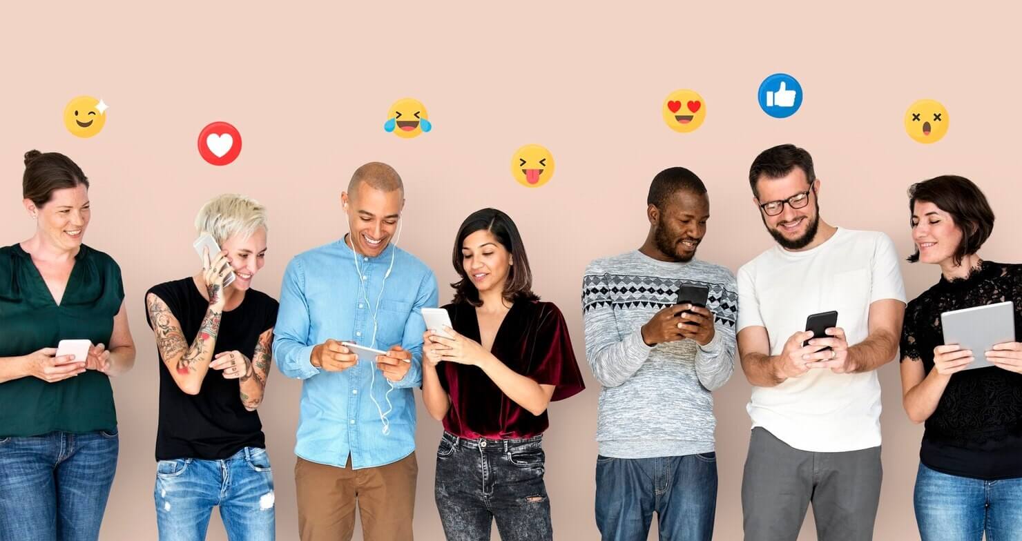 Grupo diverso de pessoas utilizando dispositivos móveis, simbolizando o conceito de "Social Listening" com emojis expressando emoções acima deles.