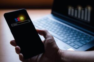 Mão segurando um celular com SEO na busca.